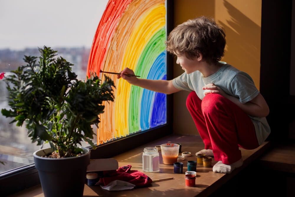 child at home draws a rainbow on the window.